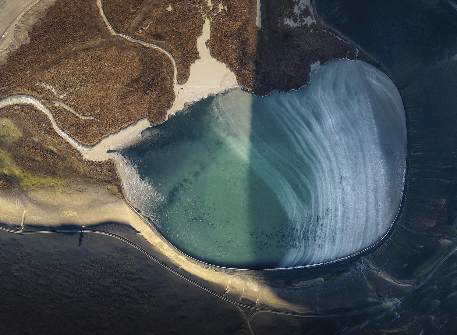 Aerial view of a turquoise, partly frozen lake among volcanic terrain in the Icelandic Highlands.