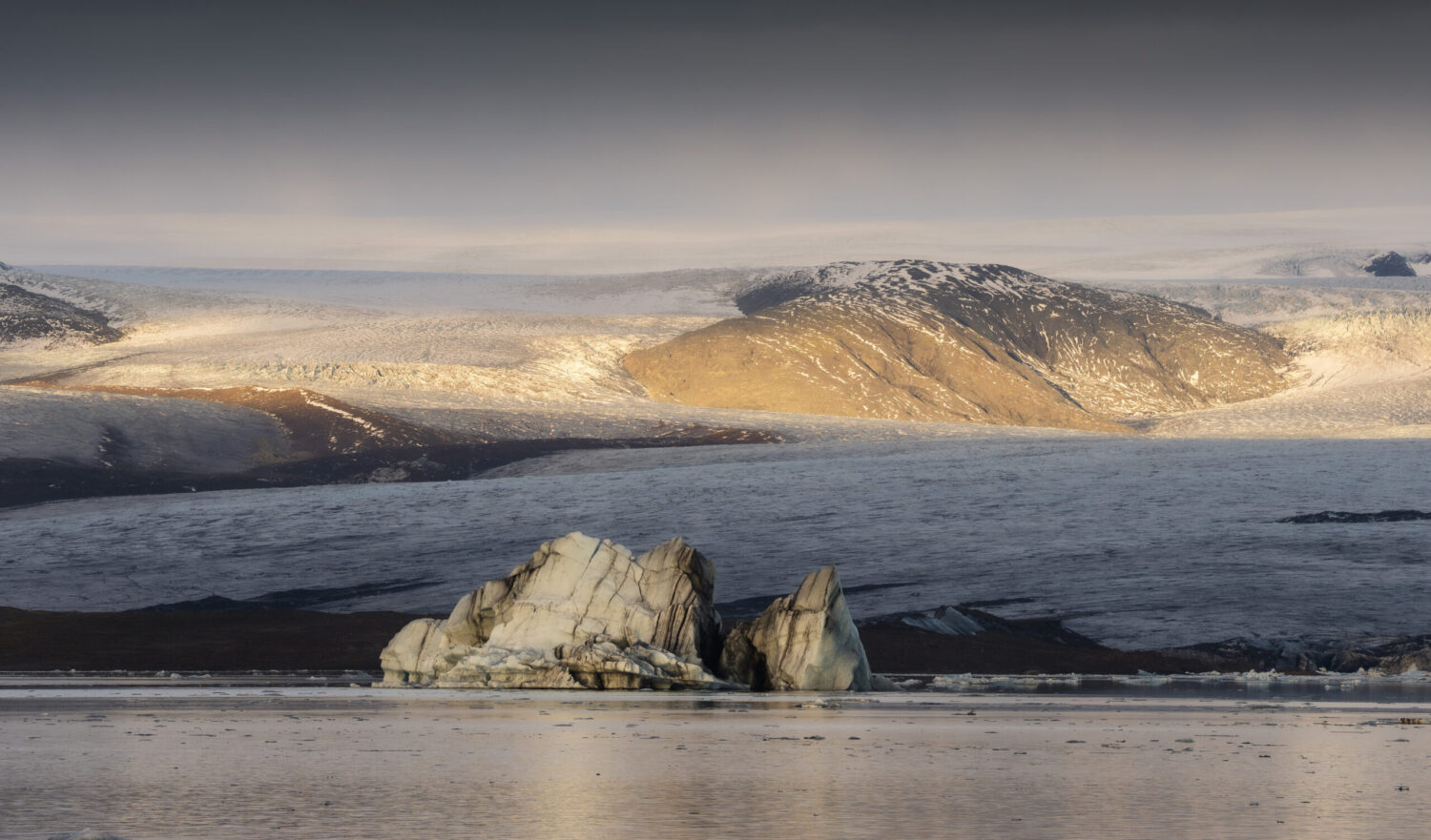 Laguna glaciale con due grandi rocce in primo piano e, sullo sfondo, un ghiacciaio sotto un cielo nuvoloso.