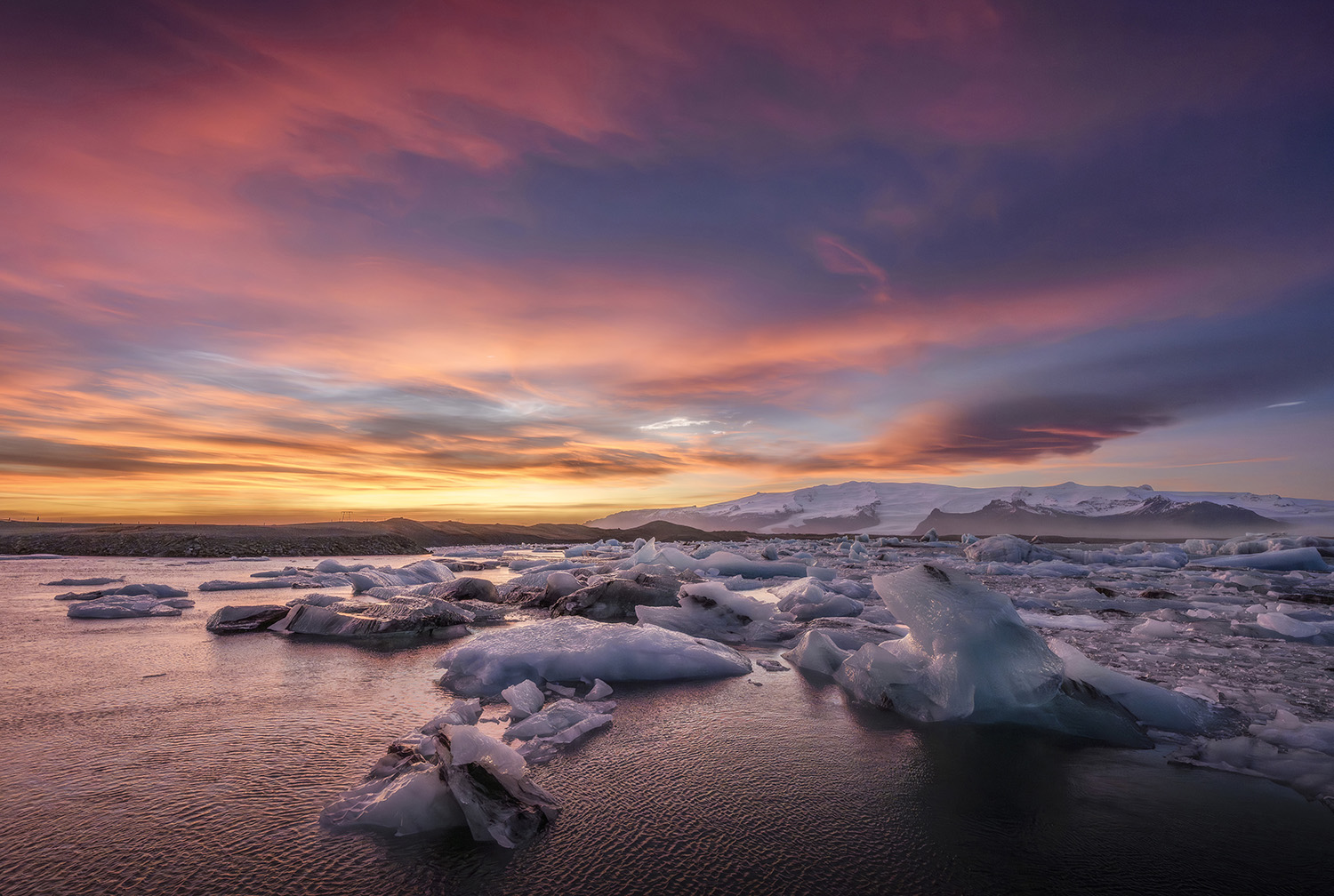 Sunset over floating ice in the Jökulsárlón glacier lagoon, under a pink and orange sky.