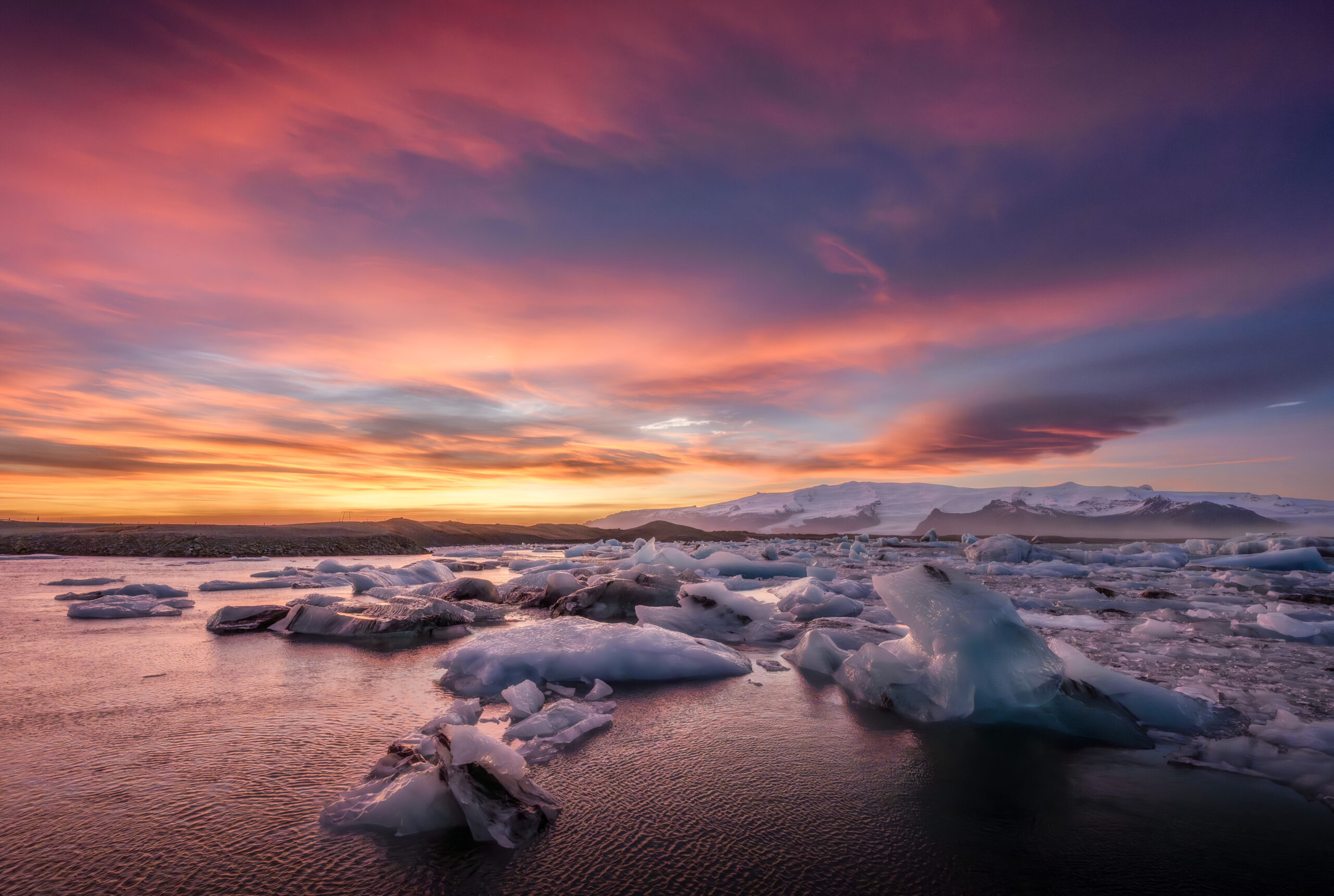 Blocchi di ghiaccio nella laguna glaciale di Jökulsárlón al tramonto, con cielo rosa e arancione e il ghiacciaio sullo sfondo.